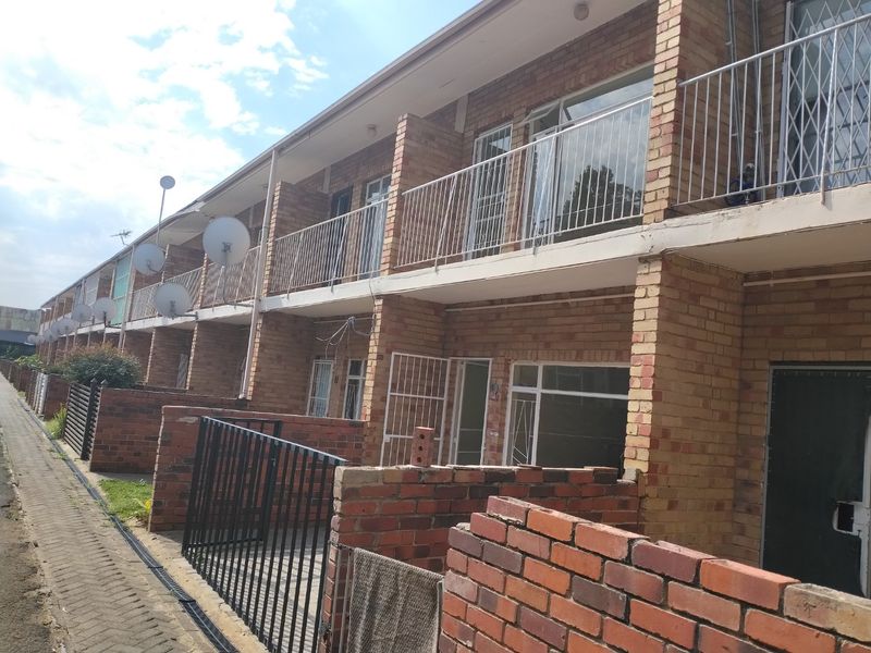 Rear view of a multi-story townhouse complex featuring face brick construction, private balcony access, and individual ground-level courtyard spaces.