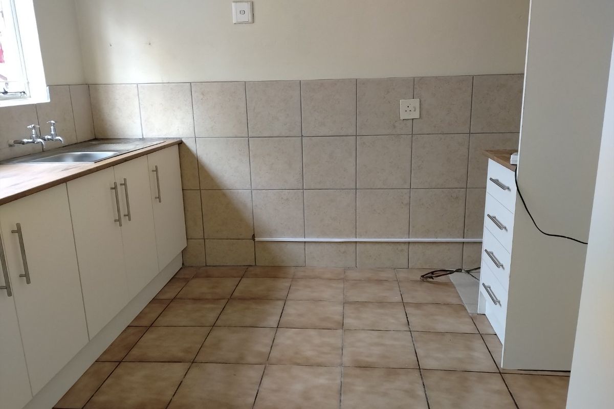 A functional, empty kitchen space featuring white cabinetry, tiled splashbacks, and a stainless steel sink, ready for personalization.