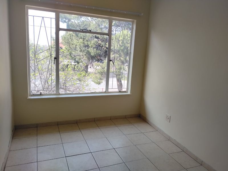 A bright, empty bedroom featuring neutral tiled flooring, a large window with security bars, and clean wall finishes.