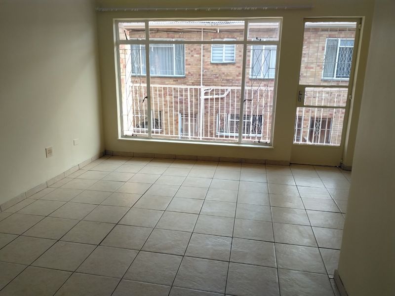 An empty, tiled living area featuring large windows and a security door, offering a bright and functional space ready for personalization.