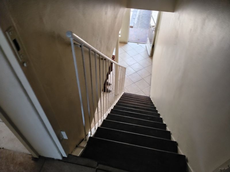 A view looking down a staircase towards the entrance, featuring tiled flooring and a metal balustrade, requiring cosmetic updates to the wall finishes.