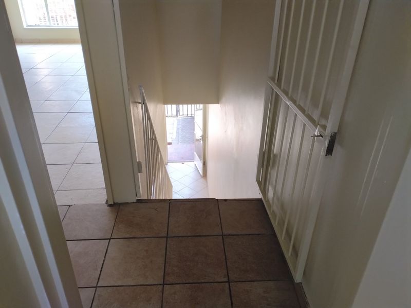 A view looking down a staircase towards an exterior entrance, featuring tiled flooring and a white security gate.