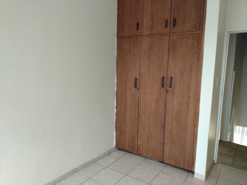 An empty bedroom featuring tiled flooring and dated built-in wooden cupboards, offering a blank canvas for potential renovation or modernization.