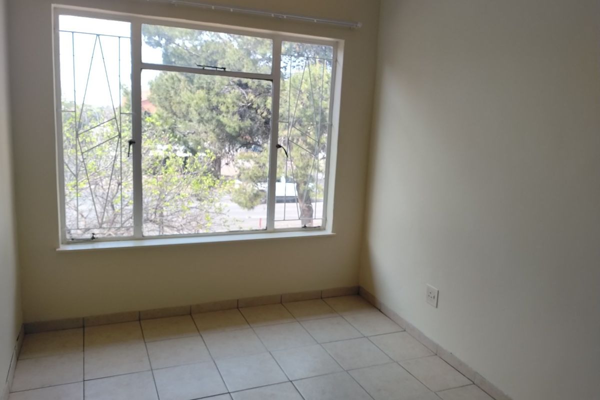 A bright, empty bedroom featuring neutral tiled flooring, large windows with security bars, and clean wall finishes, ready for personalization.