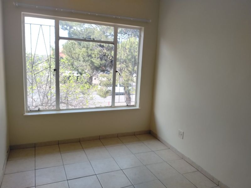 A bright, empty bedroom featuring neutral tiled flooring, large windows with security bars, and clean wall finishes, ready for personalization.