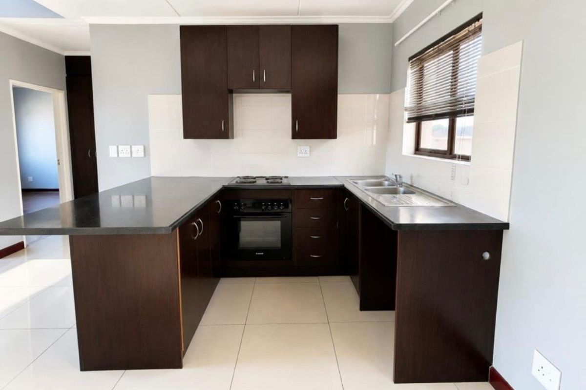 Modern kitchen featuring dark wood cabinetry, dark stone countertops, built-in oven, gas hob, and a double bowl stainless steel sink with tiled flooring.