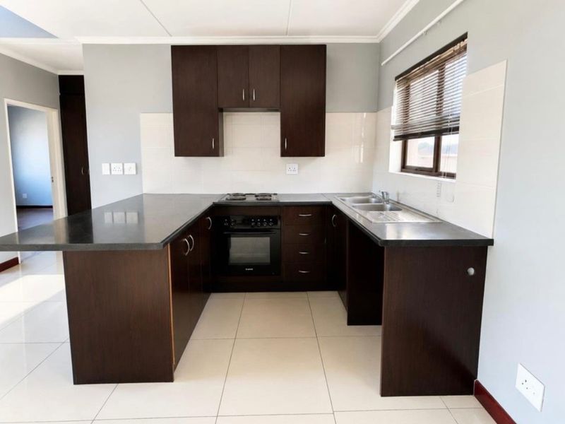 Modern kitchen featuring dark wood cabinetry, dark stone countertops, built-in oven, gas hob, and a double bowl stainless steel sink with tiled flooring.