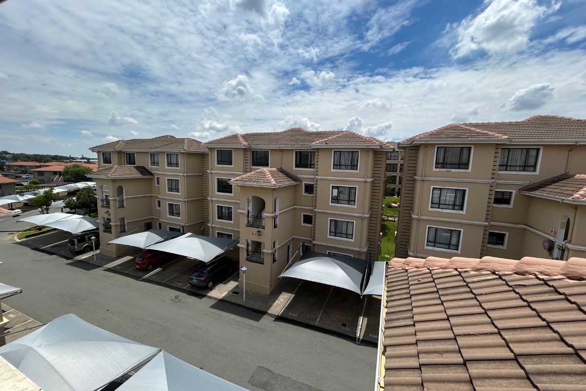 An elevated aerial view of a multi-story apartment complex featuring tiled roofs, stucco facades, and designated shade cloth parking bays.