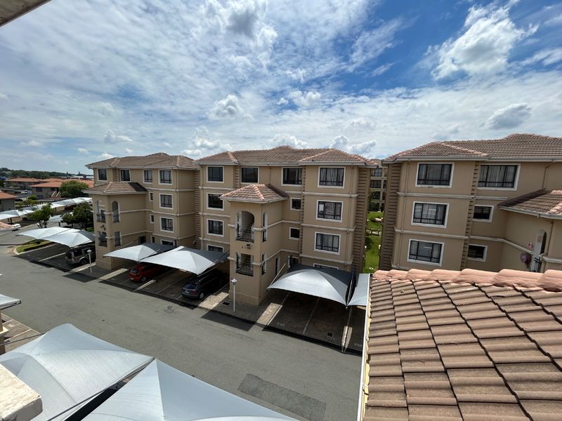 An elevated aerial view of a multi-story apartment complex featuring tiled roofs, stucco facades, and designated shade cloth parking bays.