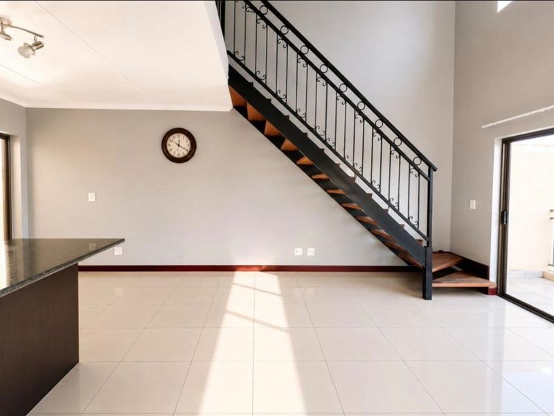 Spacious open-plan living area featuring a modern staircase with wrought iron balustrade, tiled flooring, and direct access to a balcony through sliding glass doors.