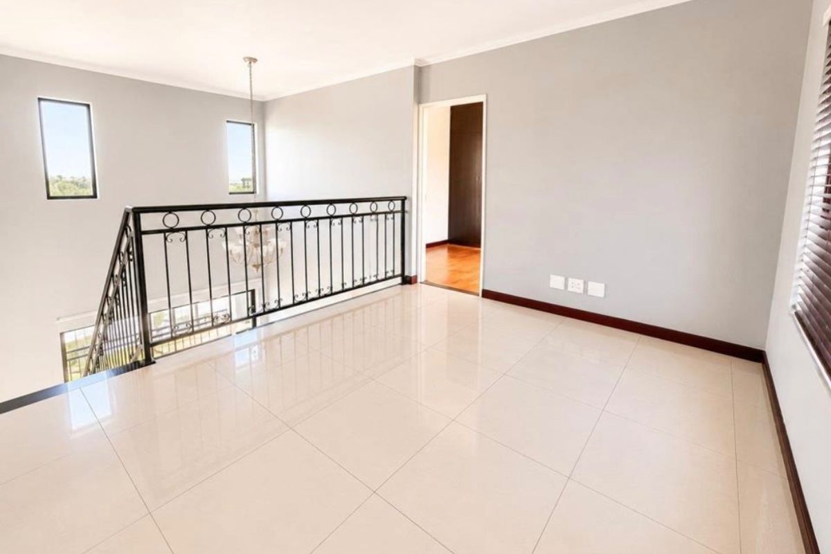 A bright, open-plan living area featuring polished tile flooring, a decorative wrought iron balustrade overlooking the lower level, and neutral wall finishes.