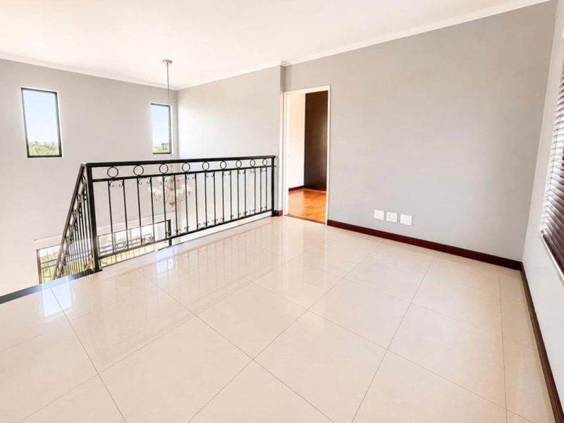 A bright, open-plan living area featuring polished tile flooring, a decorative wrought iron balustrade overlooking the lower level, and neutral wall finishes.