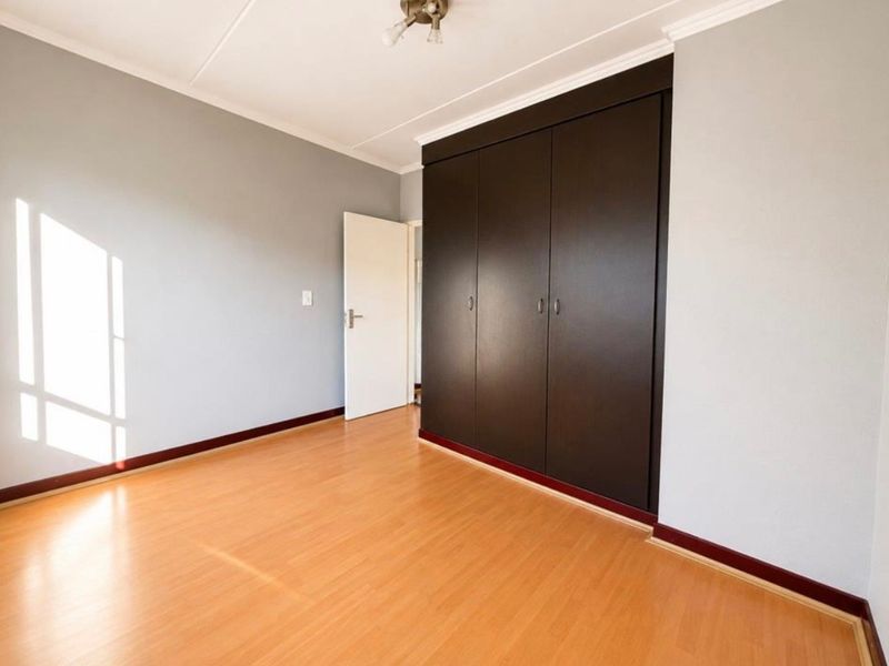 A bright, empty bedroom featuring laminate flooring, neutral walls, and dark built-in cupboards.