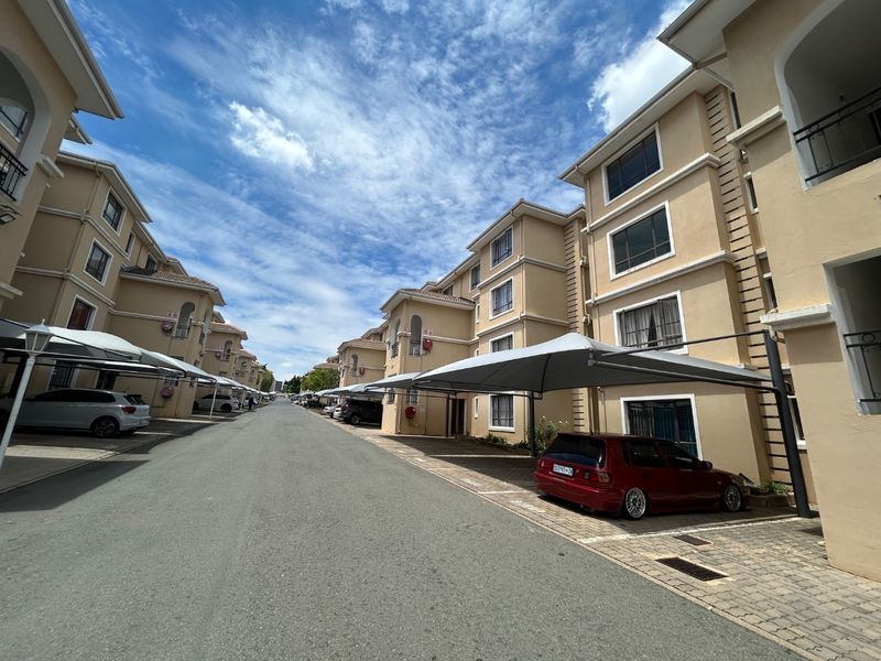 A view of the apartment complex exterior featuring multi-story residential buildings, paved driveway, and covered parking bays.
