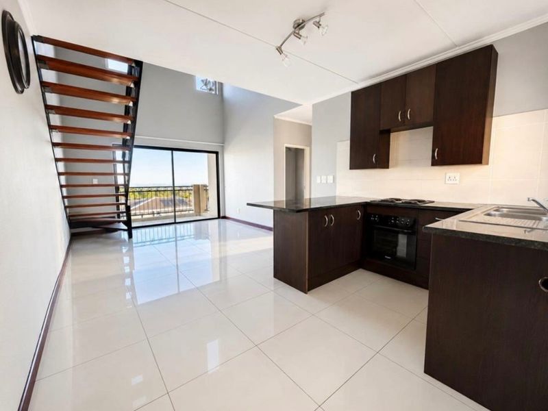 Open-plan living area featuring a modern kitchen with dark cabinetry, granite countertops, tiled floors, and a staircase leading to an upper level.