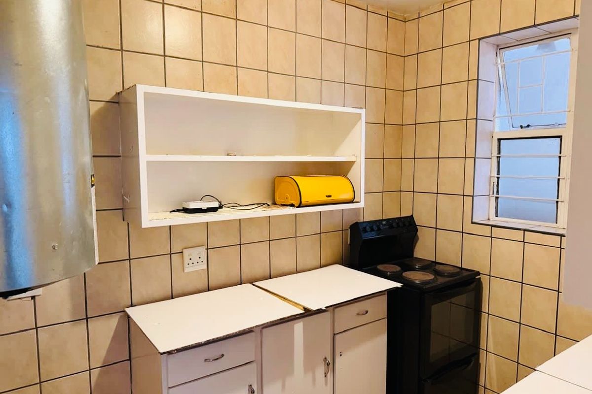 A compact kitchen featuring tiled walls, built-in cabinetry, and a freestanding stove, offering a functional space with potential for modern updates.