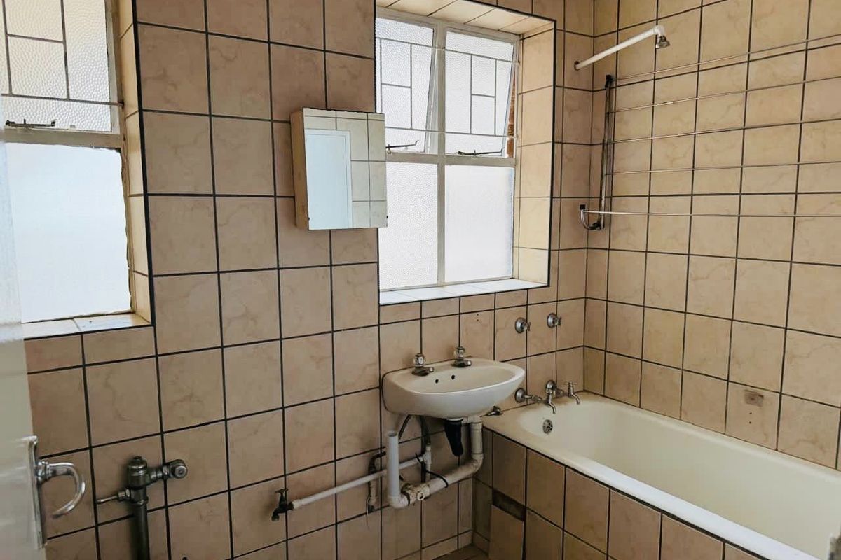 A dated bathroom featuring tiled walls, a standard bathtub, and a wall-mounted basin, requiring modernization of fixtures and finishes.