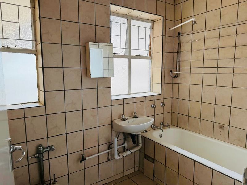 A dated bathroom featuring tiled walls, a standard bathtub, and a wall-mounted basin, requiring modernization of fixtures and finishes.