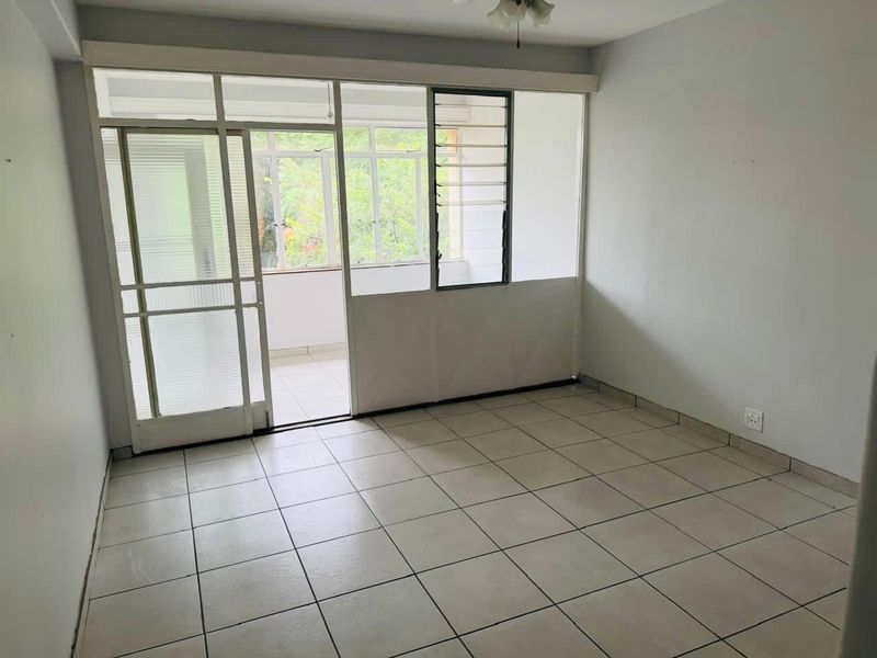 An empty living room featuring tiled flooring and direct access to an enclosed balcony through a glass sliding door.