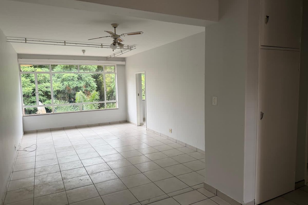 Spacious, empty living area featuring tiled flooring, a ceiling fan, and a large window with a green outlook, plus a built-in storage cupboard.