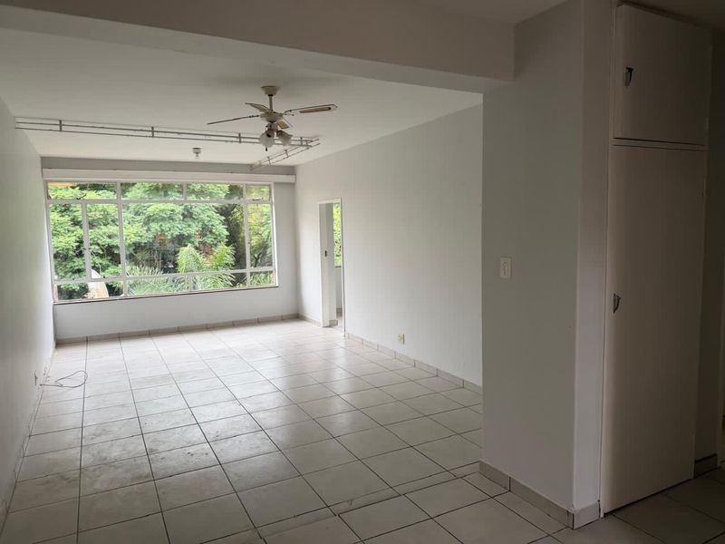 Spacious, empty living area featuring tiled flooring, a ceiling fan, and a large window with a green outlook, plus a built-in storage cupboard.