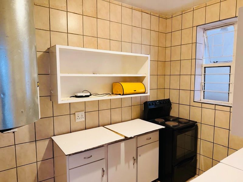 A compact kitchen featuring tiled walls, built-in cabinetry, and a freestanding stove, offering a functional space with potential for modern updates.