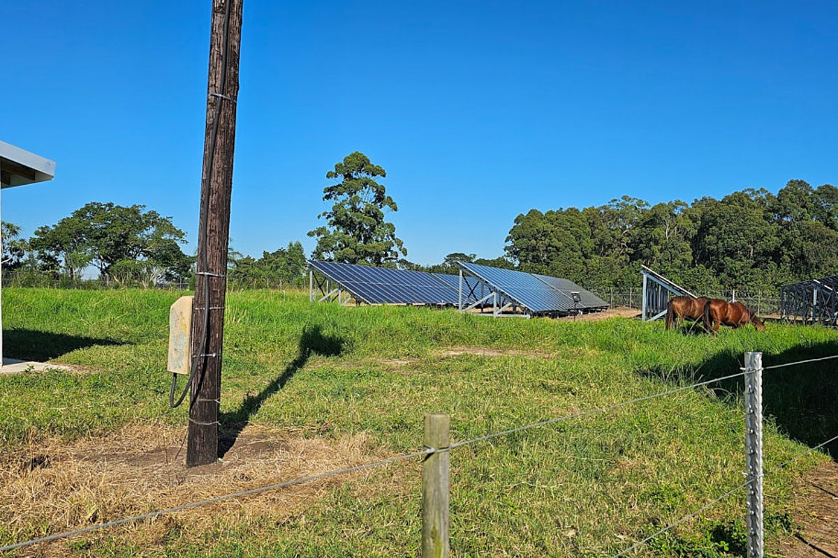 A view of the farm grounds featuring a ground-mounted solar panel array, utility infrastructure, and perimeter wire fencing.