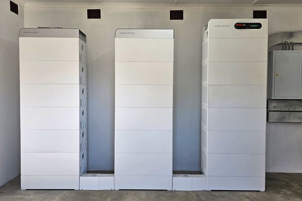 A clean utility space featuring a modern three-unit solar battery storage system and a wall-mounted electrical distribution board.