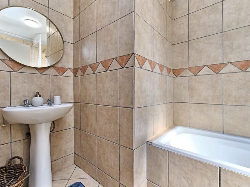 A functional bathroom featuring a pedestal basin, built-in bathtub, and full-height ceramic wall tiling with a decorative border.