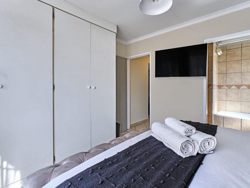 Bedroom featuring built-in cupboards and an adjoining en-suite bathroom with tiled finishes.