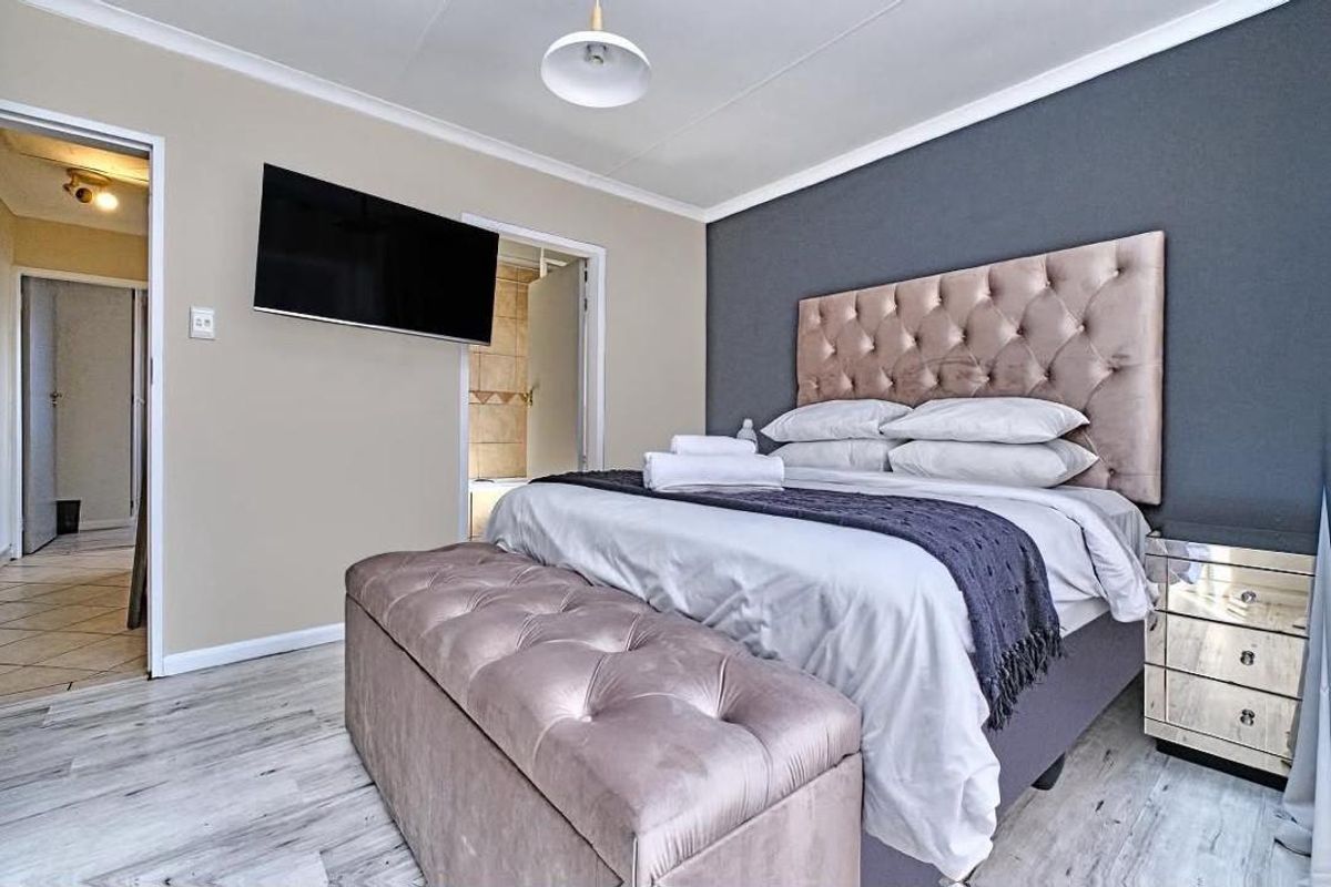 A well-maintained bedroom featuring laminate flooring, a dark accent wall, and a wall-mounted television, with direct access to an adjoining bathroom.