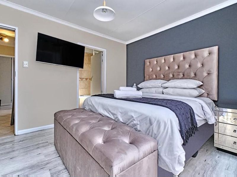 A well-maintained bedroom featuring laminate flooring, a dark accent wall, and a wall-mounted television, with direct access to an adjoining bathroom.