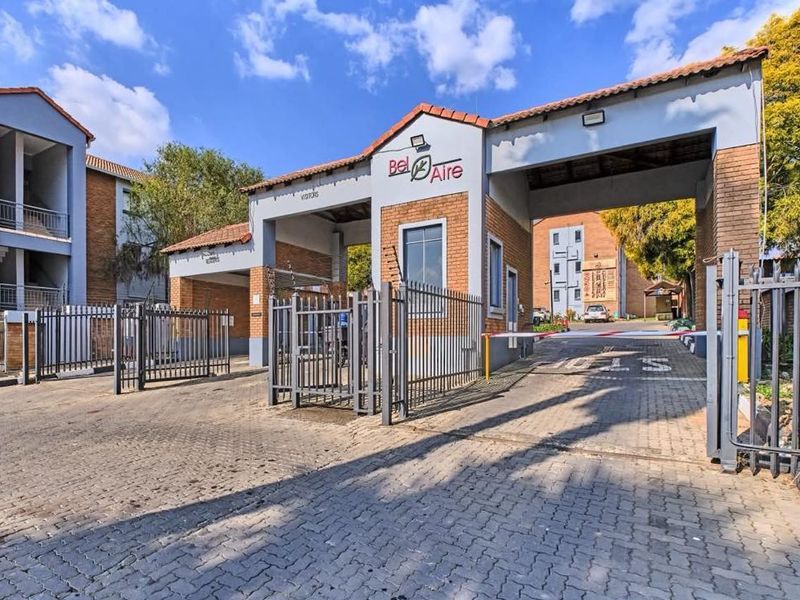 The main entrance and security gatehouse of the Bel Aire apartment complex, featuring brick construction, paved access, and controlled security barriers.