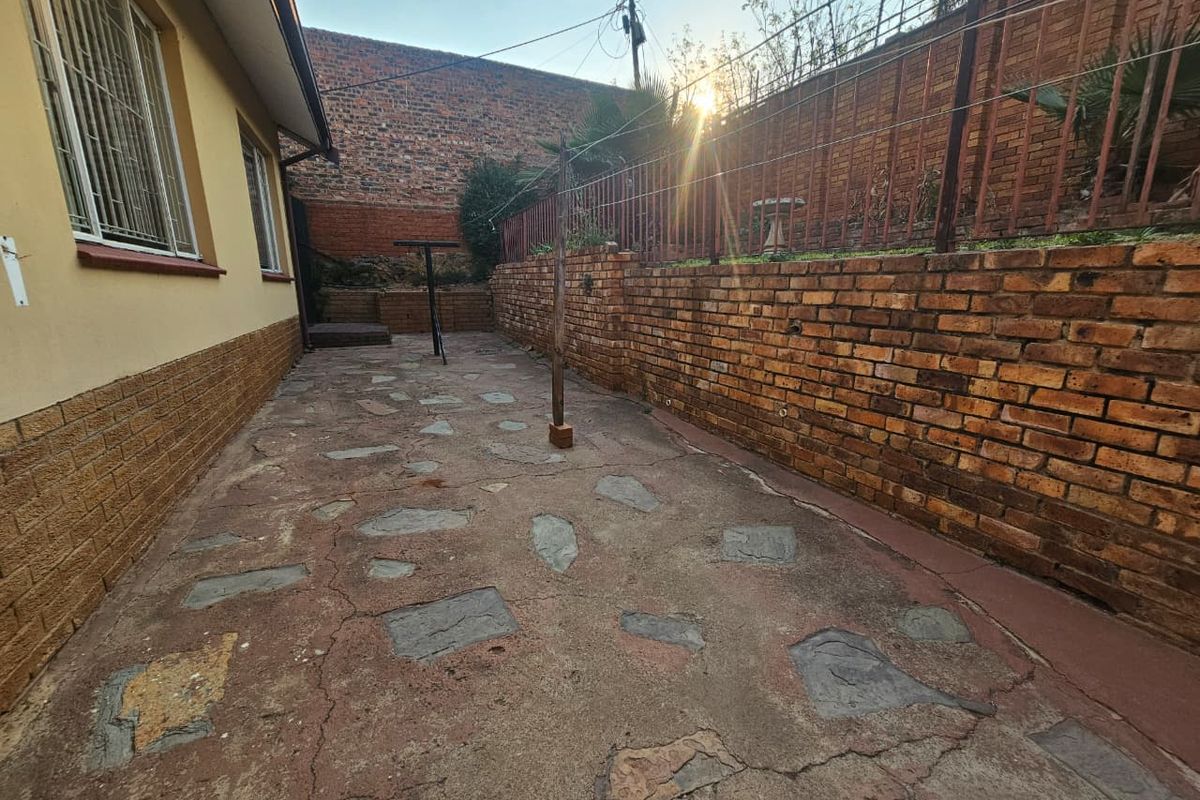 A rear exterior area featuring a brick retaining wall, crazy paving, and metal security bars on the house windows.