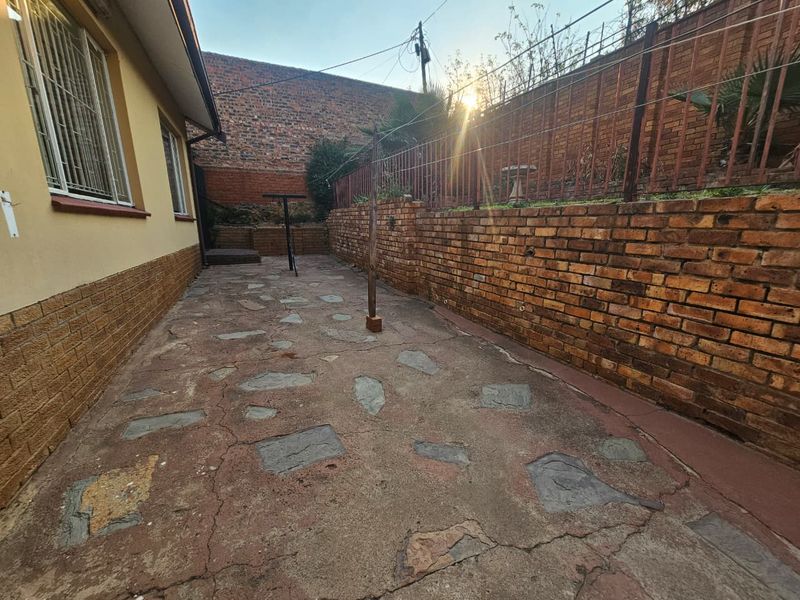 A rear exterior area featuring a brick retaining wall, crazy paving, and metal security bars on the house windows.
