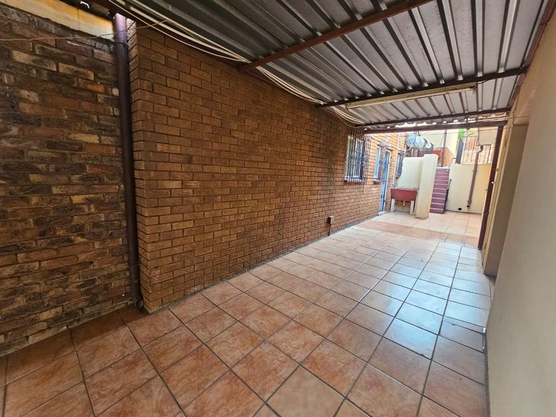 A covered outdoor patio area featuring tiled flooring, exposed brick walls, and a built-in wash basin, providing a functional utility or entertainment space.
