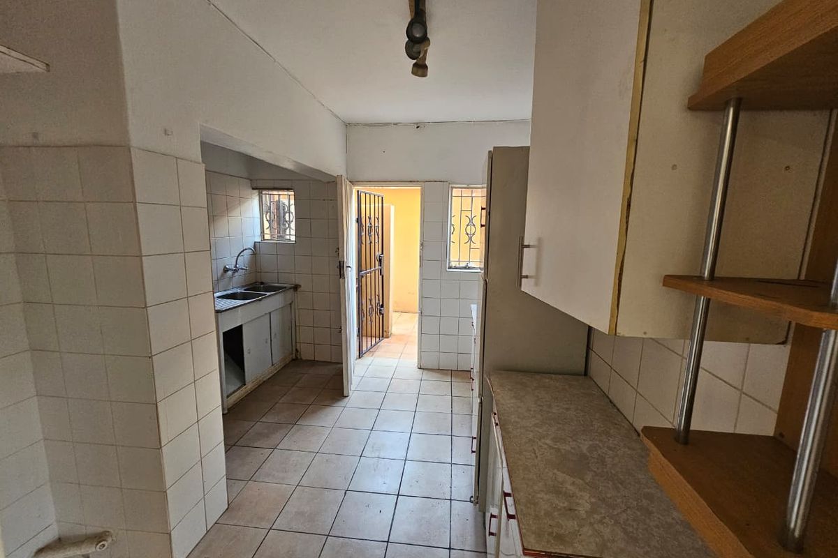 A functional kitchen space featuring tiled surfaces, built-in cabinetry, and a double sink, offering a blank canvas for potential renovation and modernization.