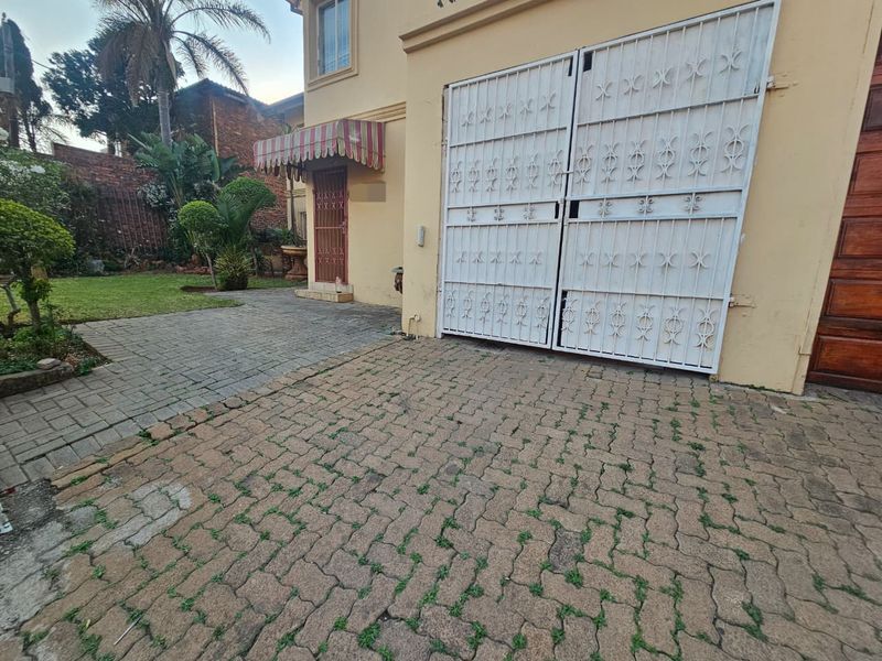 Front exterior view featuring a paved driveway, metal security gate, and a small garden area with an awning over the entrance.
