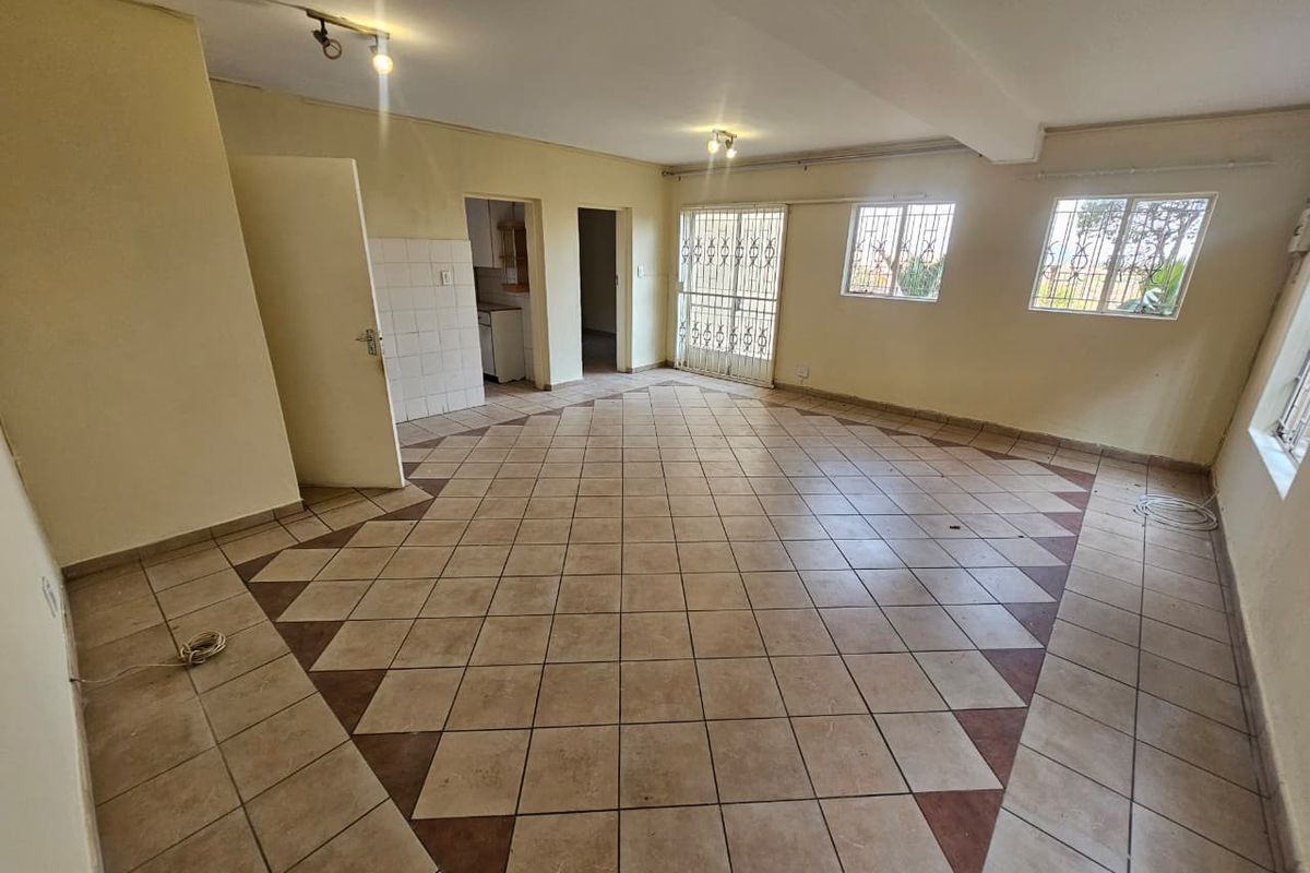 An empty, open-plan living area featuring ceramic tile flooring, security gates, and window bars, offering a blank canvas for renovation.
