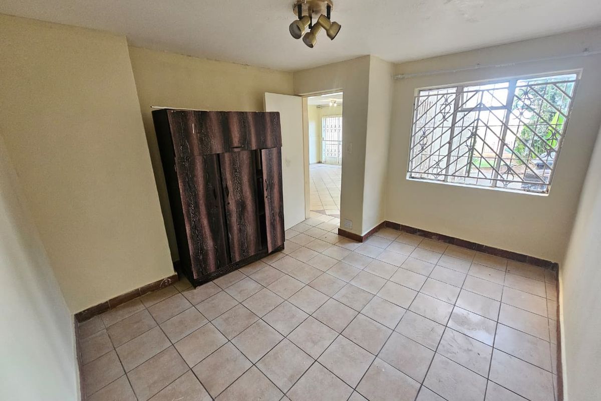 A simple bedroom featuring tiled flooring and a window with security bars, offering a blank canvas for potential renovation or restyling.