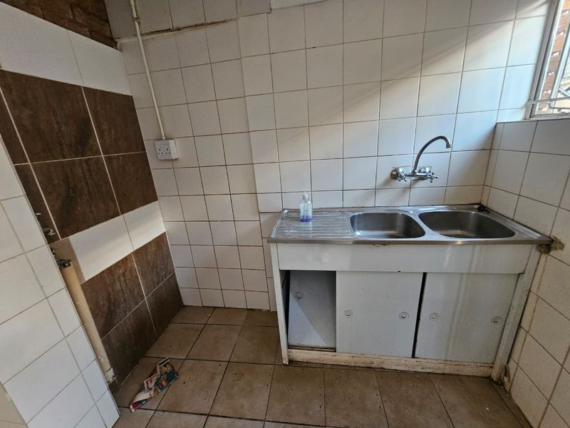 A functional laundry area featuring a double stainless steel sink, tiled walls, and tiled flooring, providing a practical space for utility tasks.
