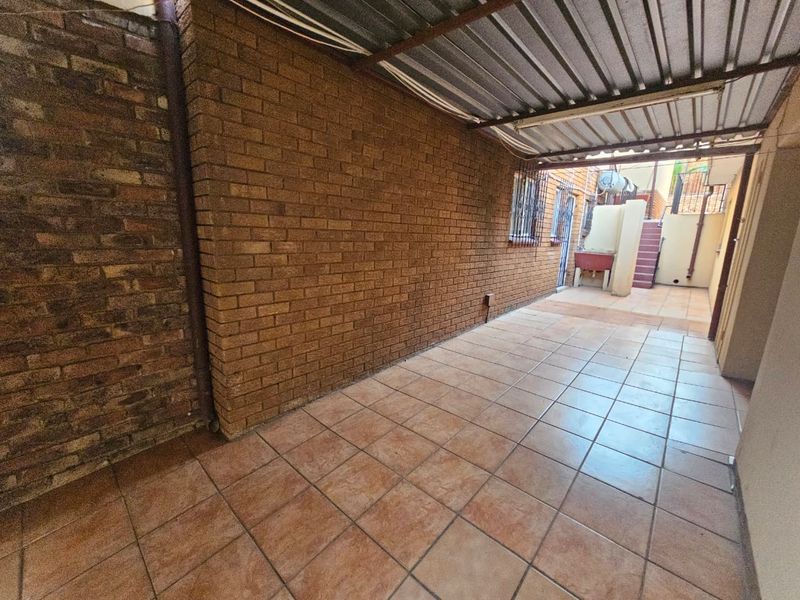 A covered outdoor patio area featuring tiled flooring, exposed brick walls, and a functional outdoor wash basin.