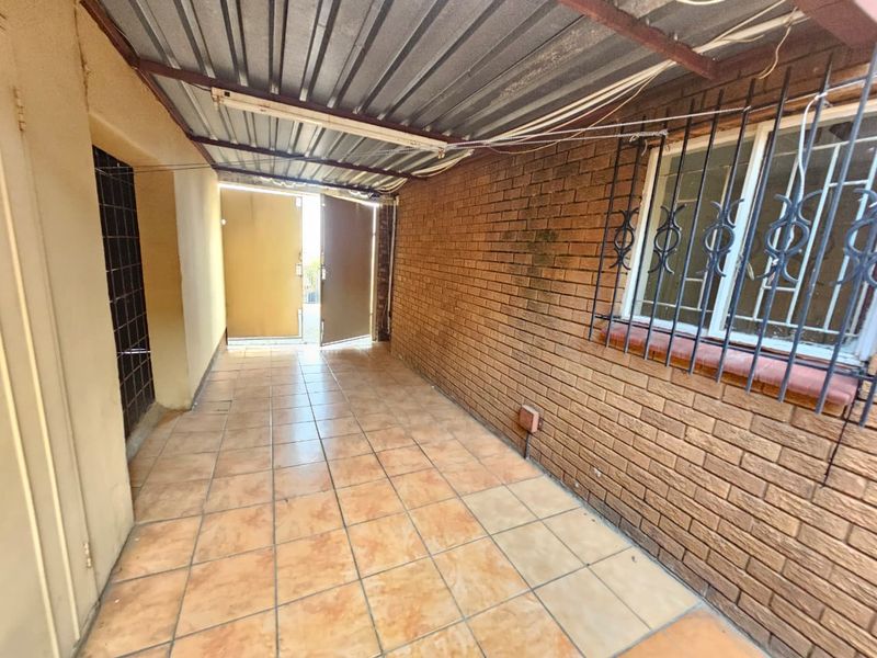 A covered outdoor patio area featuring tiled flooring, exposed brick walls, and security bars on the window, providing a functional utility or transition space.