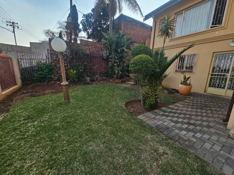 A private rear garden featuring a paved patio area, well-maintained lawn, and established landscaping, enclosed by perimeter fencing and security features.