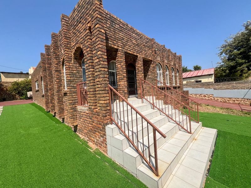 Front elevation of a face brick house featuring arched windows, a tiled entrance staircase with metal railings, and surrounding artificial lawn.