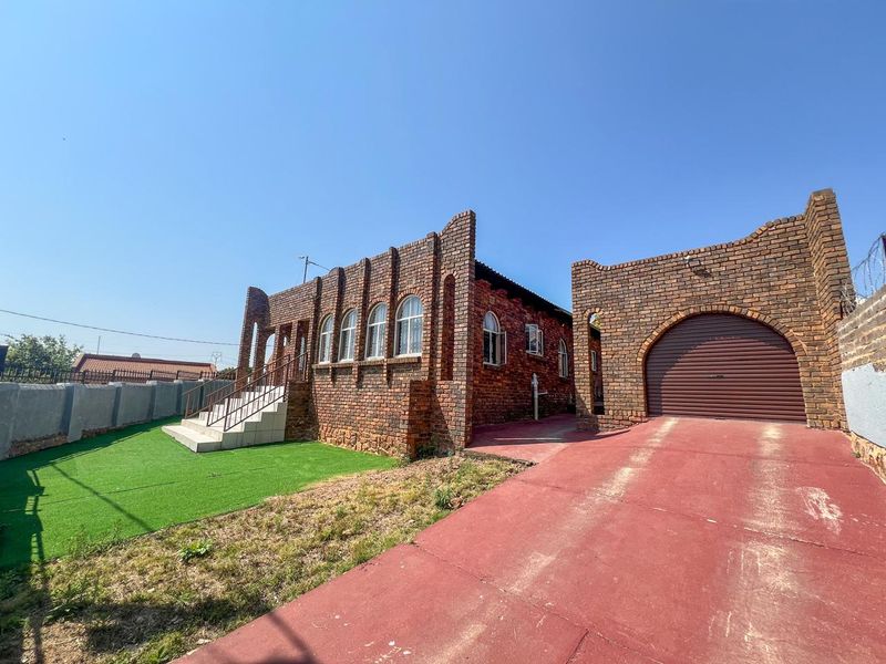 Front view of a face brick house featuring arched windows, a single roller shutter garage, and a paved driveway with an artificial lawn area.