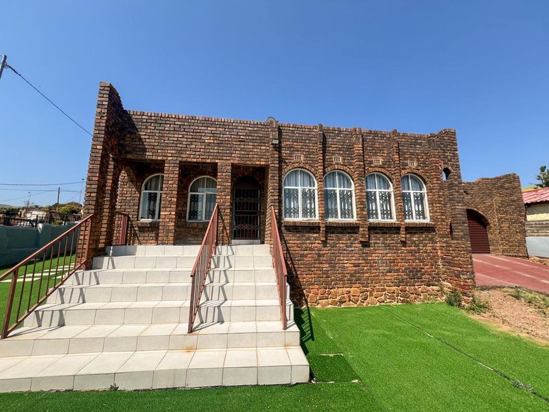 Front elevation of a face brick house featuring arched windows, a tiled entrance staircase with metal handrails, and an artificial lawn.