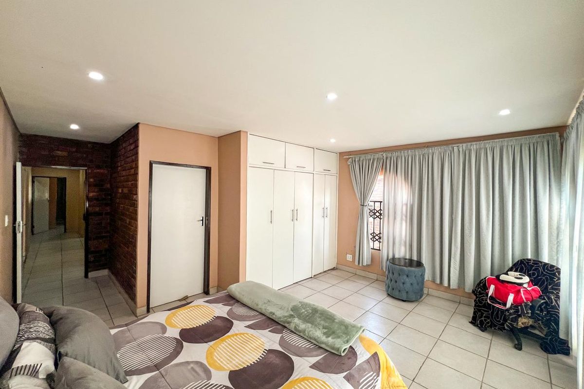 A spacious bedroom featuring tiled flooring, built-in cupboards, recessed downlights, and an exposed brick feature wall.