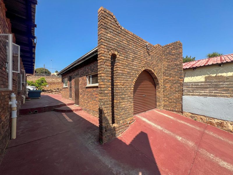 Exterior view of a face brick garage featuring a distinctive arched entrance and a roller shutter door, set on a paved driveway.