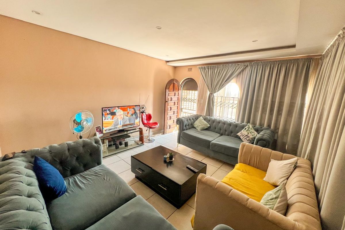 A comfortable living room featuring tiled flooring, recessed ceiling lights, and an arched wooden entrance door with security gate.